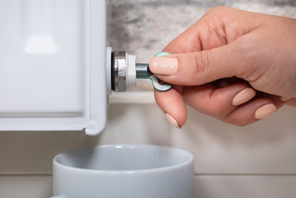 Close-up Of A Person's Hand Turning Radiator Bleed Valve To Release Air With Cup