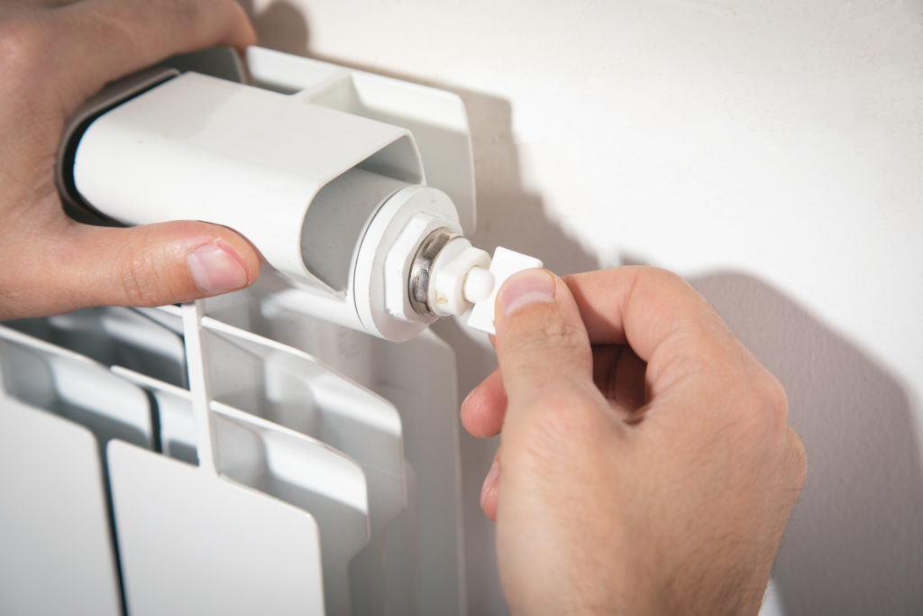 A man bleeding a radiator using a radiator valve key.