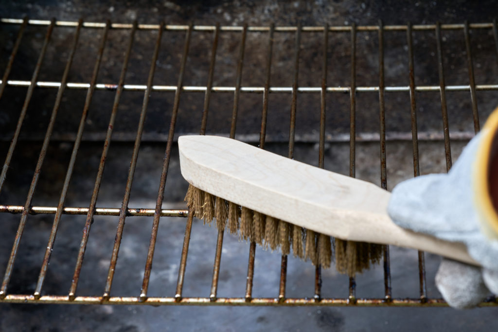 Wooden wire brush cleaning a barbeque grill from rust