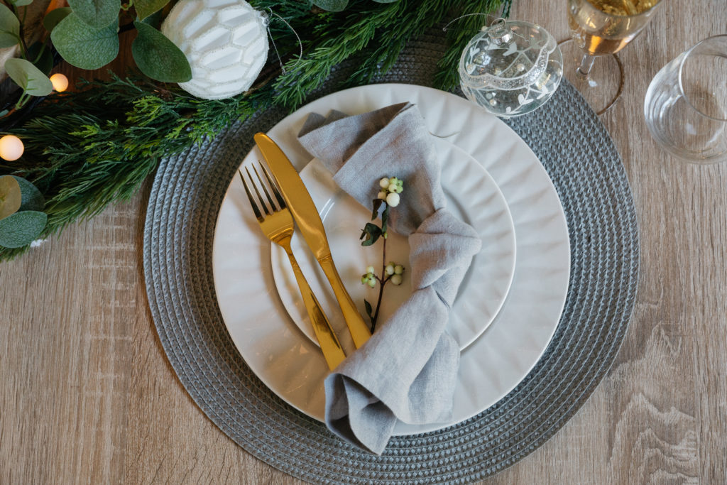 A white table setting with grey place mat and gold cutlery