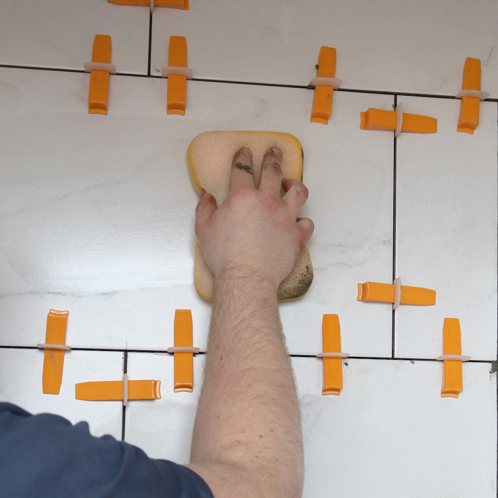 A yellow sponge being used to to remove excess grout from tiles