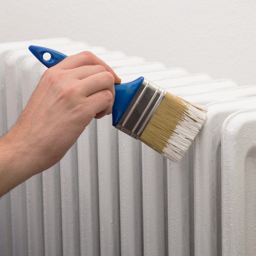 A white radiator being painted with a blue paint brush